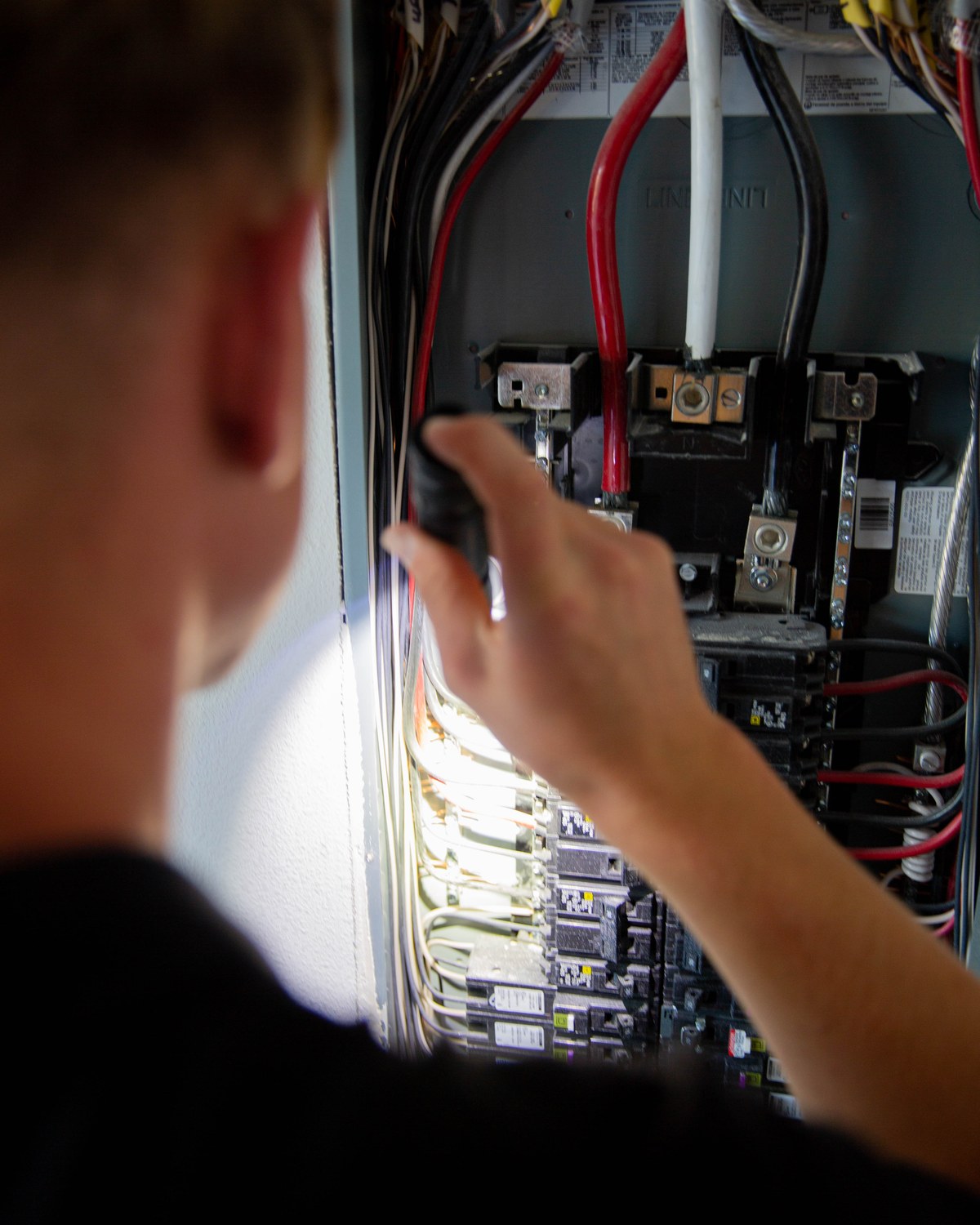Sam Belza examining breakers and wiring inside an accessible electrical panel